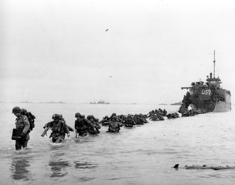 FILE - U.S. reinforcements wade through the surf from a landing craft in the days following D-Day and the Allied invasion of Nazi-occupied France at Normandy in June 1944 during World War II. On D-Day, Charles Shay was a 19-year-old Native American army medic who was ready to give his life — and actually saved many. Now 99, he's spreading a message of peace with tireless dedication as he's about to take part in the 80th celebrations of the landings in Normandy that led to the liberation of France and Europe from Nazi Germany occupation. (Bert Brandt/Pool via AP, File)