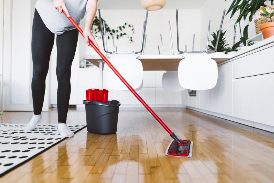 A person in black leggings and white socks mops a hardwood floor.