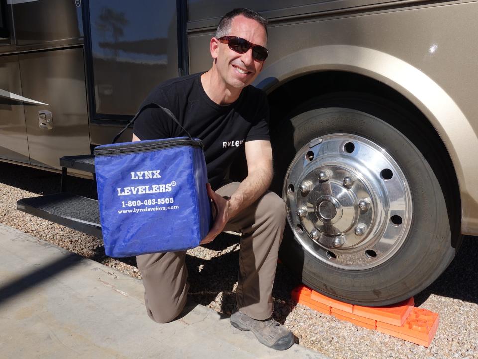 Marc holding Tri-Lynx Levelers that come in a ten pack with a handy storage bag while kneeling next to the RV with the blocks on a tire