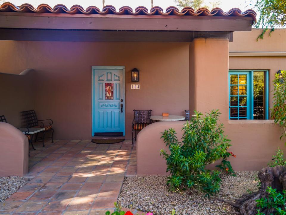 A tan adobe home with a blue door and blue window trimmings