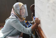 Teacher Inggit Andini, wearing a face shield as a precaution against the coronavirus outbreak, teaches at a makeshift class at her home in Tangerang, Indonesia, Monday, Aug. 10, 2020. Andini offered free extra lessons for students who lack access to the internet as the school where she works at remain closed and switched to online learning due to the outbreak. (AP Photo/Tatan Syuflana)