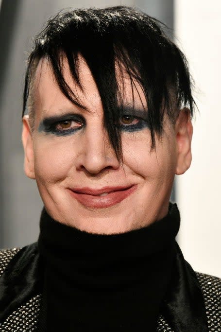 Marilyn Manson, wearing a black turtleneck and patterned blazer, smiles at a celebrity event