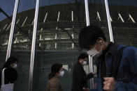 People with masks walk past a building reflecting the New National Stadium, a venue for the opening and closing ceremonies at the Tokyo 2020 Olympics, Sunday, Feb. 23, 2020, in Tokyo. (AP Photo/Jae C. Hong)