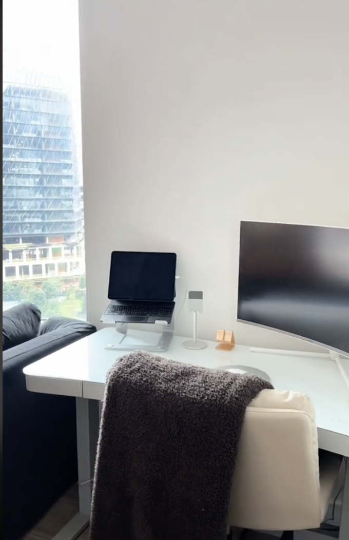 Home office setup with a laptop on a white desk, a monitor to the side, and a city view outside the window