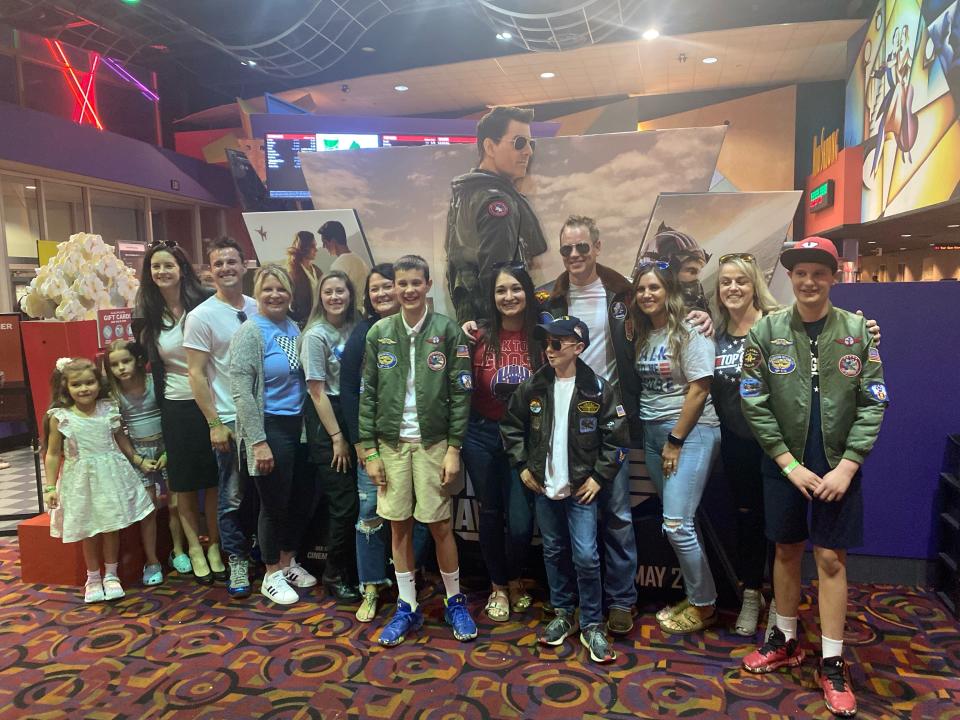 Chris Dickes (center, wearing aviator sunglasses) poses with his friends and family members in front of a poster for "Top Gun: Maverick," where he appeared as an extra.