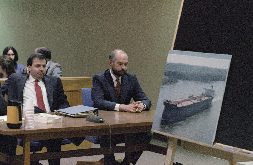 FILE - Fired Exxon Valdez skipper Joseph Hazelwood, right, sits with his lawyer Michael Chalos as a photograph of the tanker is displayed on an easel in Anchorage Superior Court, March 20, 1990. Hazelwood, the captain of the Exxon Valdez oil tanker that ran aground more than three decades ago in Alaska, causing one of the worst oil spills in U.S. history, has died in July 2022, the New York Times reported. He was 75. (AP Photo/Jack Smith, File)