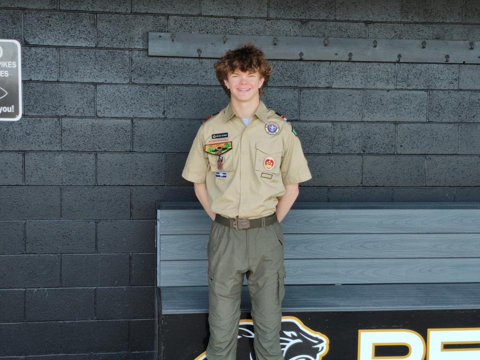 Perry baseball player Bryan Witmer poses in his Boy Scout uniform next to a dugout bench he helped build for his Eagle Scout project.