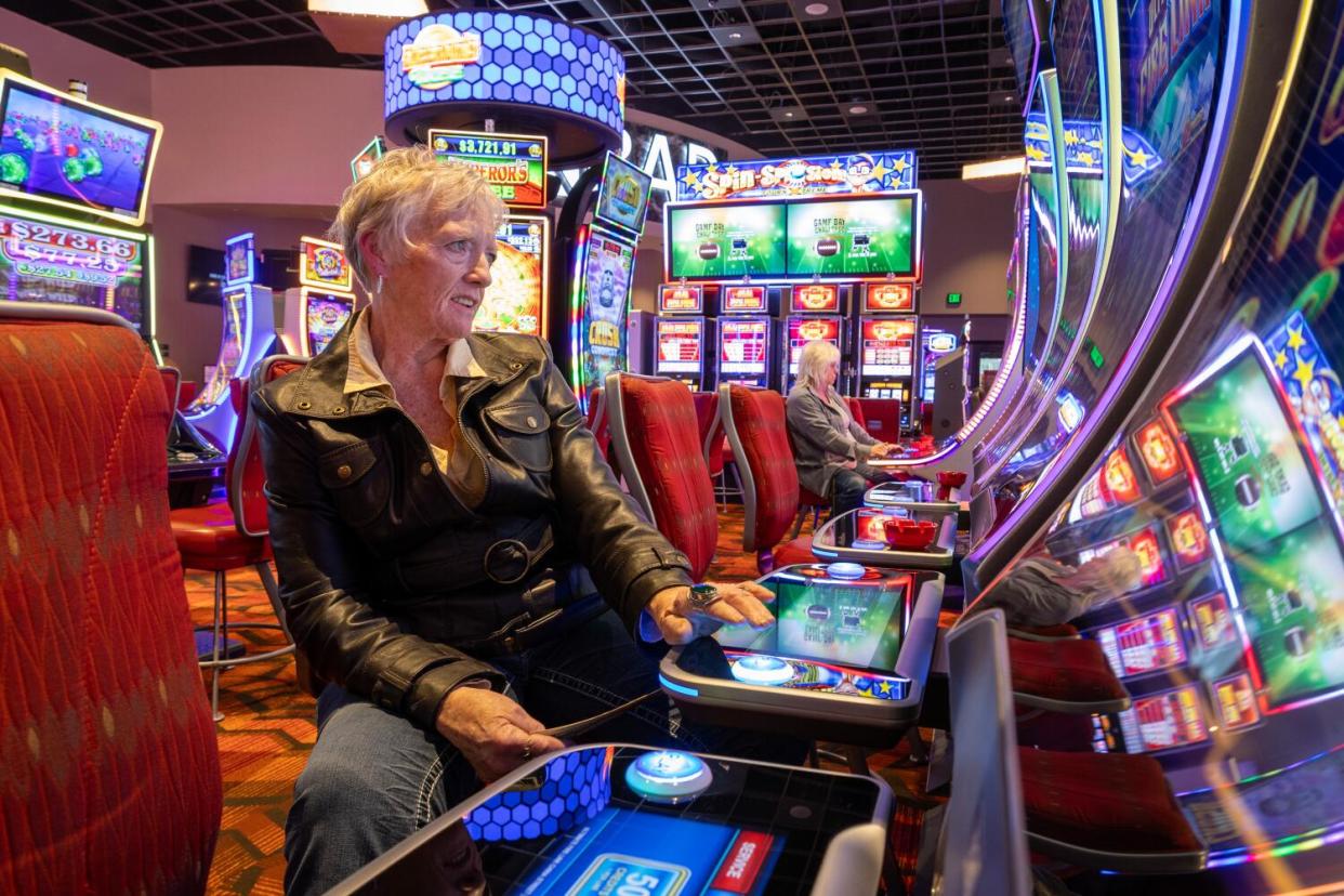 A woman in a leather jacket plays slots.
