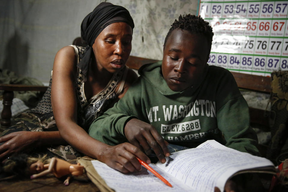 FILE - In this Saturday, Sept. 26, 2020 file photo, Miriam Nyambura coaches her son Peter Kihika, 16, who wants to become a teacher but now works during the day scavenging materials to be sold for recycling at Kenya's largest landfill Dandora, after his mother lost her job and his school was closed due to the coronavirus pandemic, in Nairobi, Kenya. As schools reopen in some African countries after months of lockdown, relief is matched by anxiety over everything from how to raise tuition fees amid the financial strain wrought by the COVID-19 pandemic to how to protect students in crowded classrooms. (AP Photo/Brian Inganga, File)