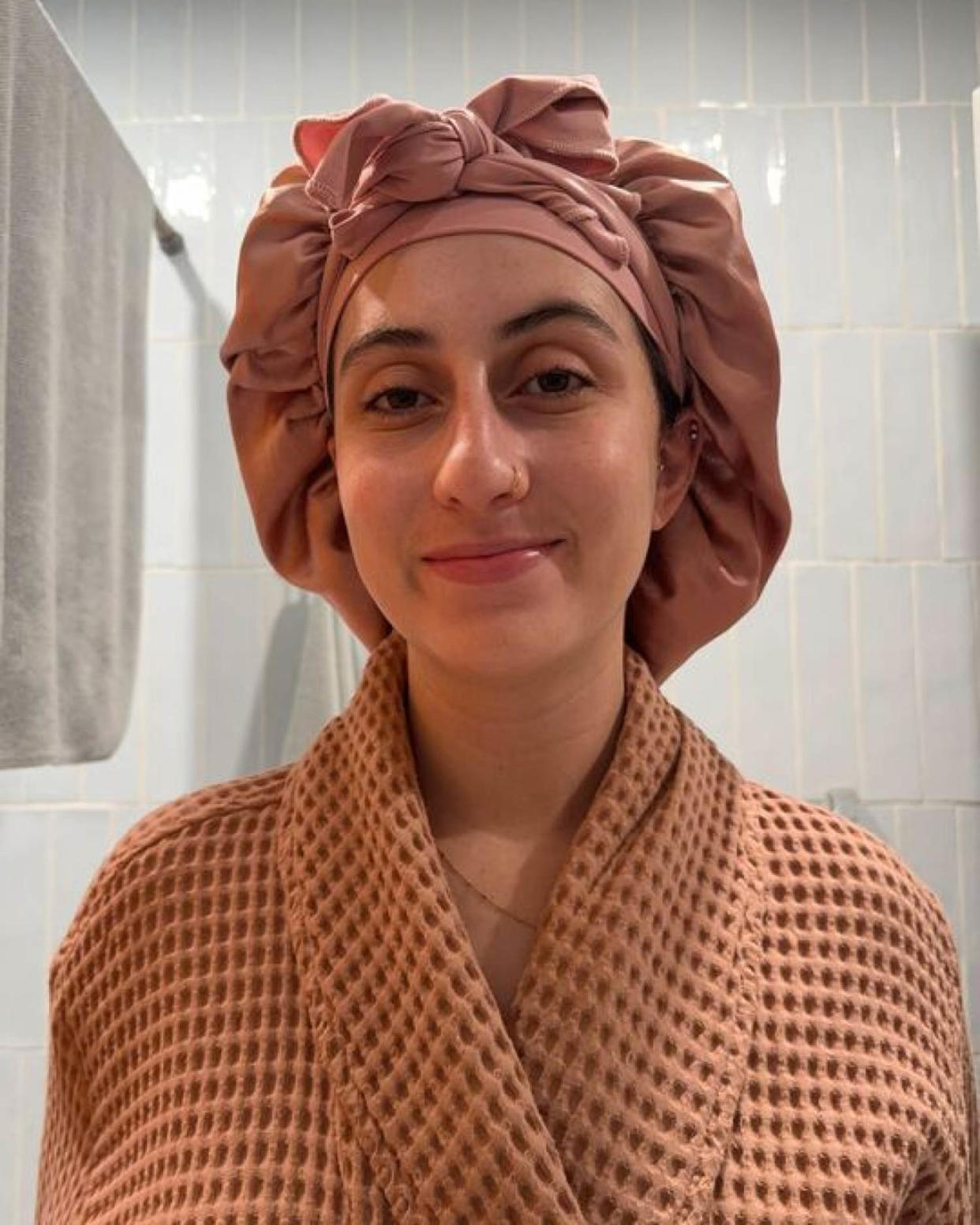 Woman wears a robe and a terracotta-colored Yanibest Satin Bonnet tightly wrapped around her head in her bathroom. (Courtesy Rebecca Rodriguez)