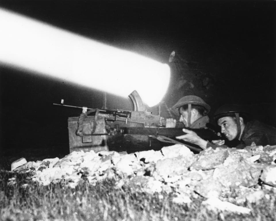 FILE - With a searchlight beam piercing through the night, a machine gunner and a rifleman are on alert as the British Canadian offensive drive continues, in July 1944, south of Caen, in the Normandy region of France. The D-Day invasion that helped change the course of World War II was unprecedented in scale and audacity. Veterans and world dignitaries are commemorating the 79th anniversary of the operation. (Pool via AP, File)