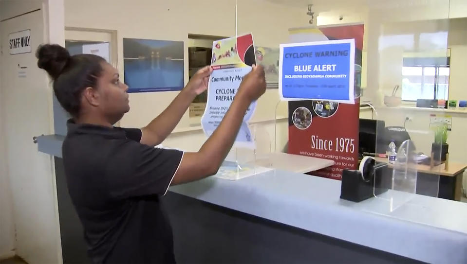 This image made from a video, shows a woman sticking up a poster advising of a community meeting next to a blue alert poster in Broome, Australia Wednesday, April 12, 2023. Miners, cattle ranchers, tourists and Indigenous locals were evacuating from Australia’s remote northwest coast on Wednesday as an intensifying tropical cyclone approached. (Australian Broadcasting Corporation via AP)