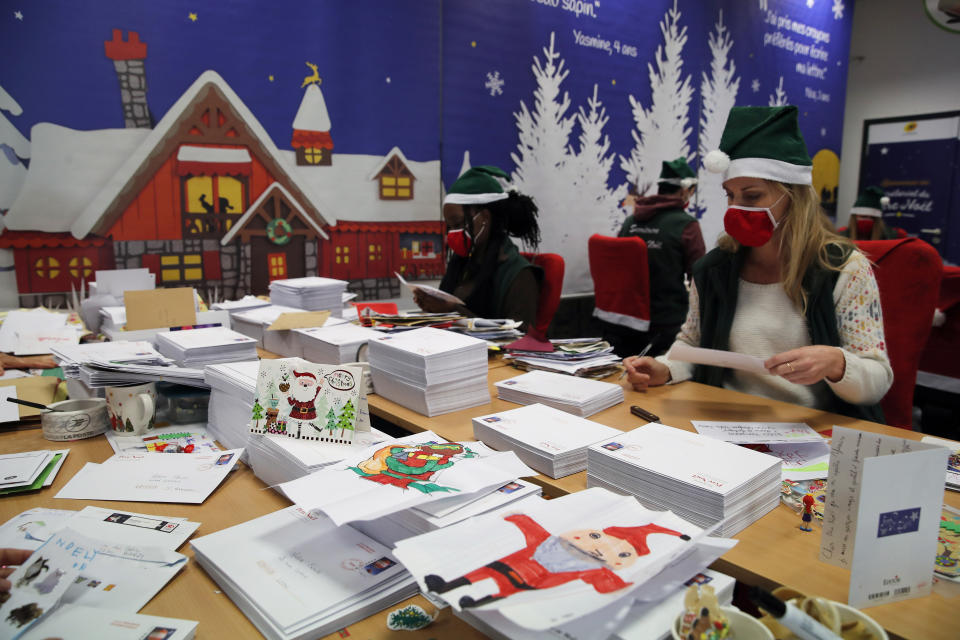 Postal workers who call themselves "Elves" open envelopes addressed "Pere Noel" - Father Christmas in French - decorated with love hearts, stickers and glitter, in Libourne, southwest France, Monday, Nov. 23, 2020. Letters pouring by the tens of thousands into Santa's mailbox offer a glimpse into the worries and hopes of children awaiting a pandemic-hit Christmas. Along with usual pleas for toys and gadgets, kids are also mailing requests for vaccines, for visits from grandparents, for life to return to the way it was. The office estimates that one letter in three mentions the pandemic. (AP Photo/Francois Mori)