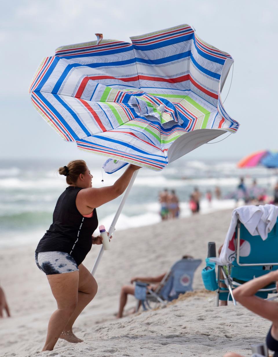 A woman catches a beach umbrella before it blows away in Seaside Park on July 18, 2022.