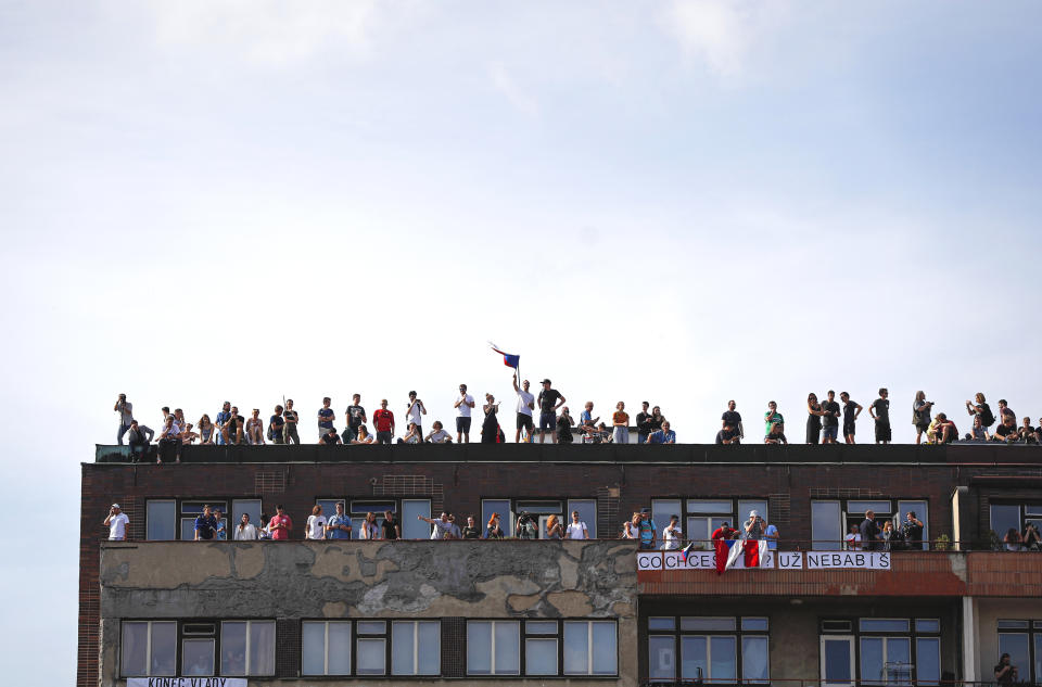 People watch from a nearby building as protesters demand the resignation of Czech Prime Minister Andrej Babis in Prague, Czech Republic, Sunday, June 23, 2019. Protesters are on calling on Czech Prime Minister Andrej Babis to step down over fraud allegations and subsidies paid to his former companies. (AP Photo/Petr David Josek)