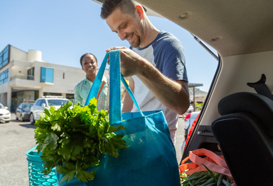 people putting reusable grocery bags full of fresh food into the back of their car