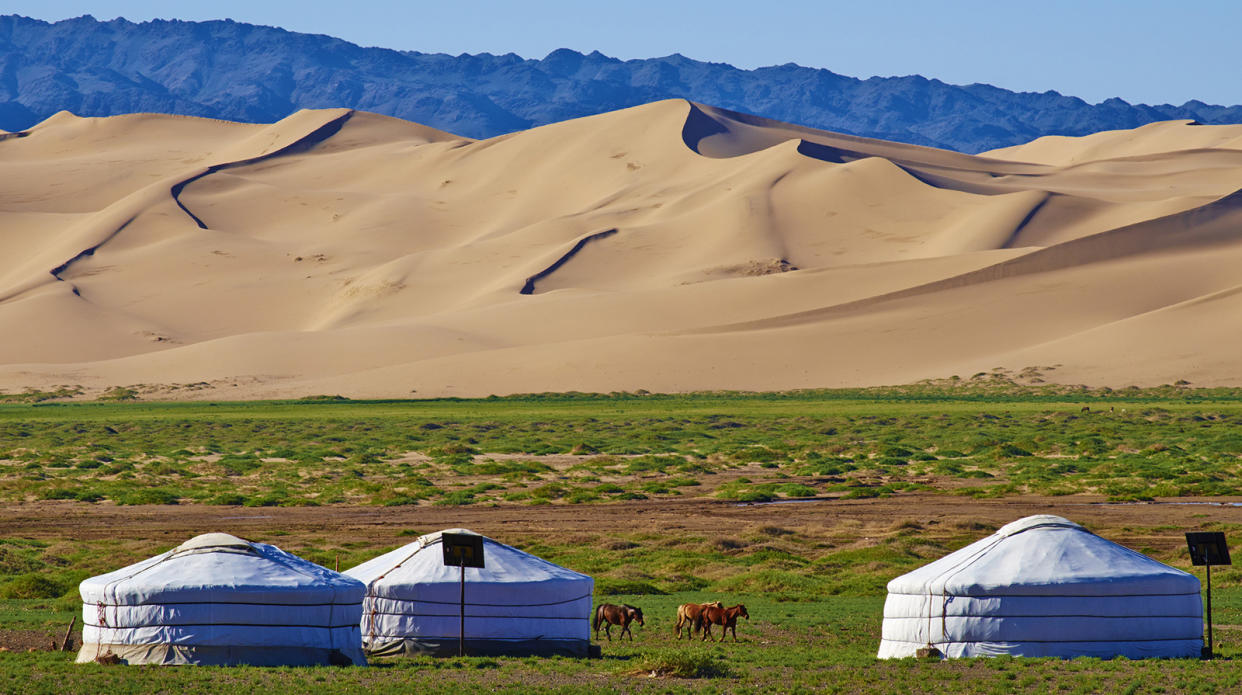 Yurts on patchy grass with sand dunes and desert mountains in the background