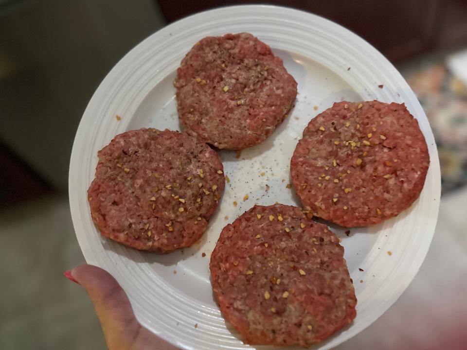 hand holding a plate of raw burger patties