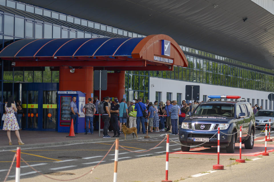 Security personnel and an explosive sniffing dog stand at the entrance of the departures terminal as passengers wait in line at the international airport in Chisinau, Moldova, Tuesday, Aug. 16, 2022. Over the last two months non-European Union Moldova, which shares a border with war-torn Ukraine, has been plagued by scores of bomb threats that have wreaked havoc on the resources of the already overstretched authorities.(AP Photo/Cristian Straista)