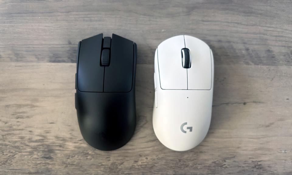 A black Razer Viper V3 Pro gaming mouse and a white Logitech G Pro X Superlight 2 gaming mouse lie next to each other on a brown wooden table.