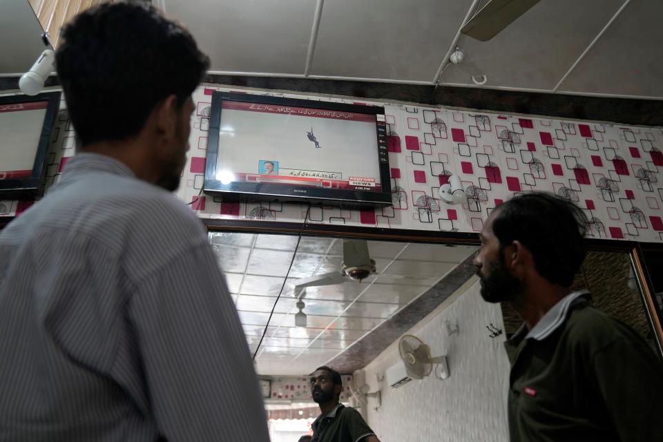 People were watching a news channel broadcasting information about the rescue, at a barber shop in Lahore (AP Photo/K.M. Chaudary)