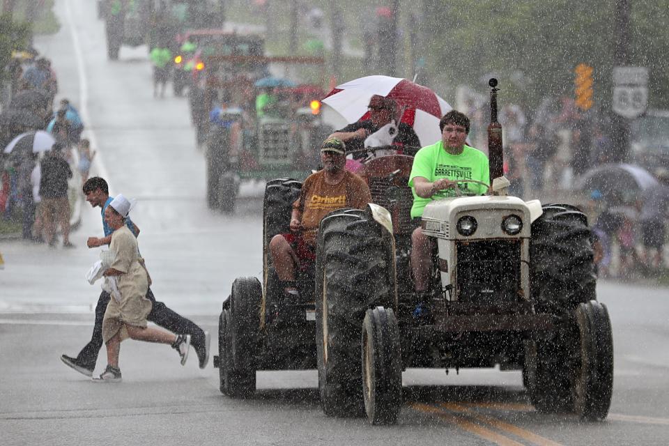 An unfortunate tractor owner makes his way up North Street as an Amish couple scurries to find relief from the rain during the Garrettsville Tractor Parade, Saturday, June 29, 2024, in Garrettsville, Ohio.