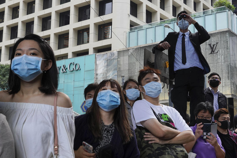 FILE - In this Nov. 12, 2019 file photo, people wearing face masks watch pro-democracy protesters in Central, Hong Kong. In 2019, face masks were the signature of Hong Kong’s protesters, who wore them to protect against tear gas and conceal their identities from authorities. These same masks are now ubiquitous around the world -- a hallmark of the spreading coronavirus worn by people from China and Iran, to Italy and America, seeking to protect against the new coronavirus. The vast majority of people recover from the new virus. (AP Photo/Vincent Yu, File)