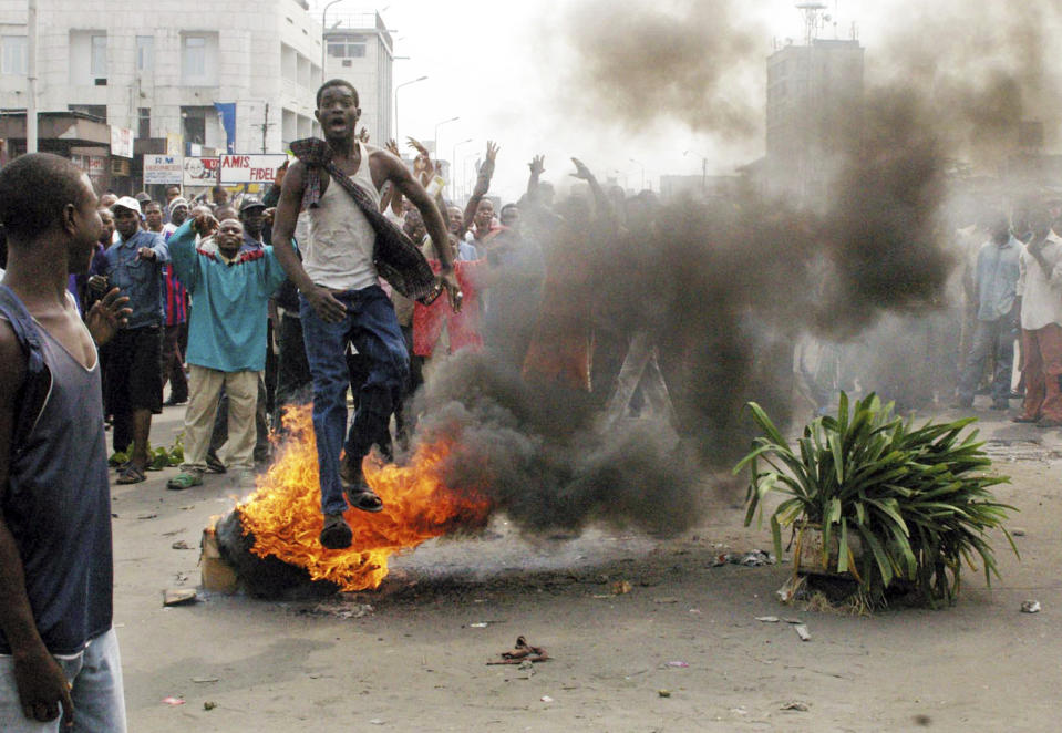 FILE - In this Thursday, June 30, 2005 file photo shot by AP contributing photographer John Bompengo, a demonstrator leaping over a burning tire in the Victoire neighbourhood of the capital Kinshasa, Democratic Republic of Congo. Relatives say longtime Associated Press contributor John Bompengo has died of COVID-19 in Congo's capital. Bompengo, who had covered his country's political turmoil over the course of 16 years, died Saturday, June 20, 2020 at a Kinshasa hospital. (AP Photo/John Bompengo, file)