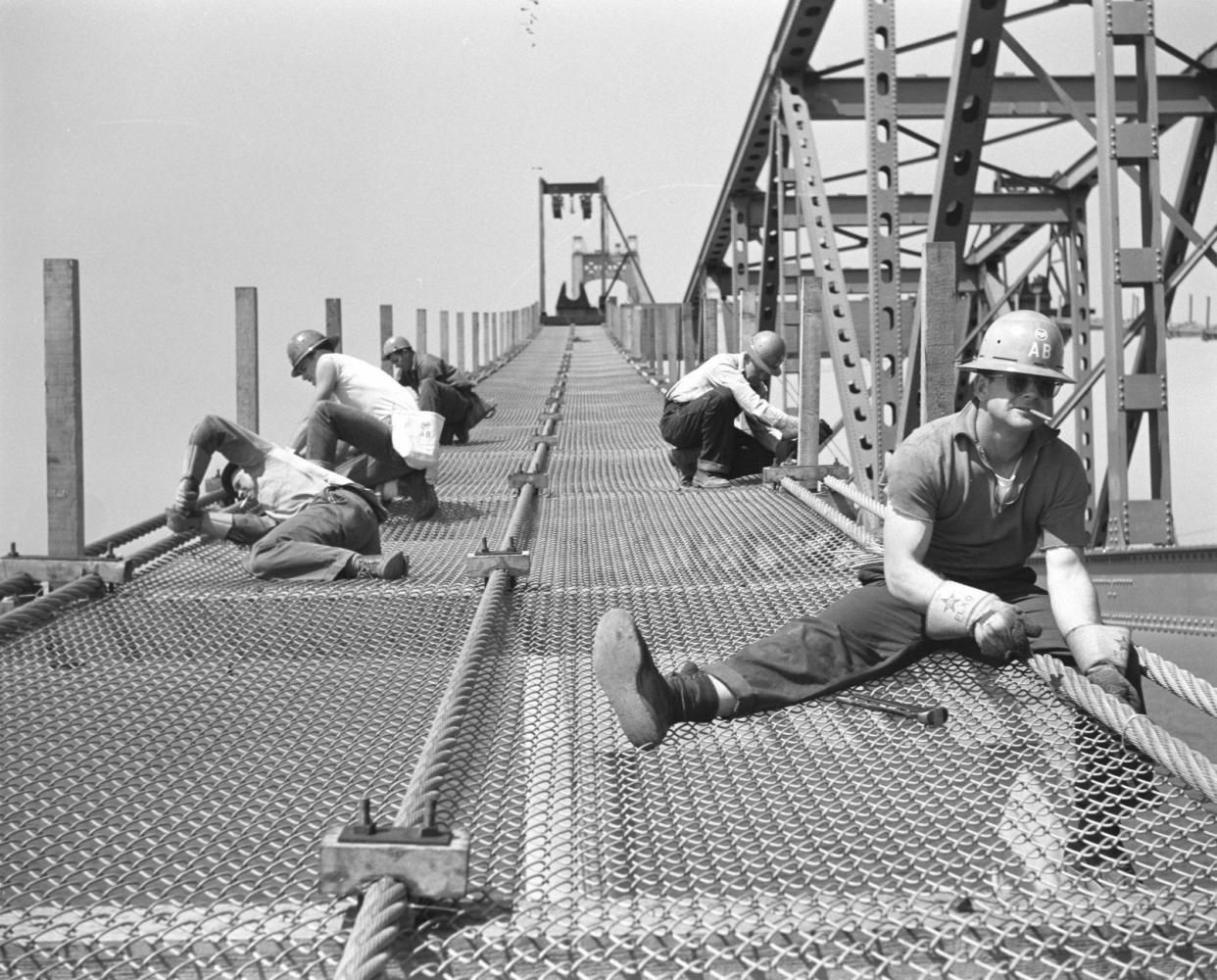 Jack R. Thompson (far right) works as part of a crew wiring the mesh to catwalk ropes between piers 17 and 18 on the Mackinac Bridge in 1956. Thompson says it was a pencil in his mouth, “not a smoke.”