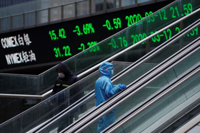 Pedestrian in protective suit rides an escalator near an overpass with an electronic board showing stock information in Shanghai