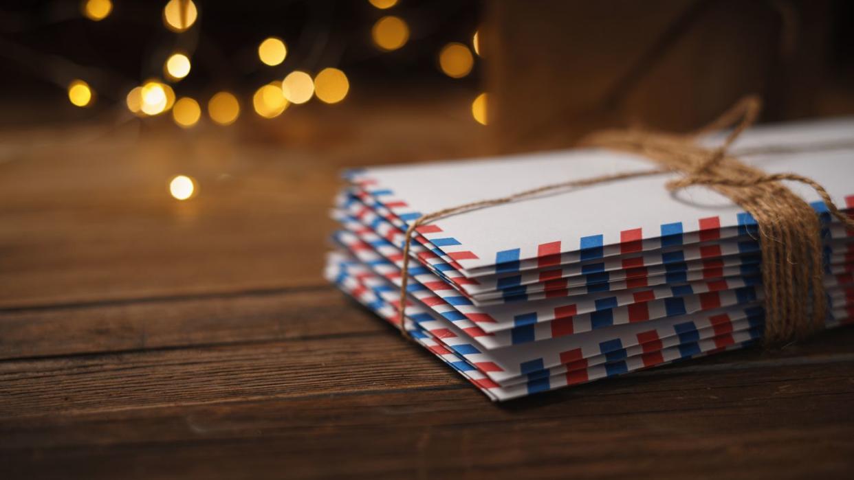 front view of many letter envelopes stacked one on top of the other on a rustic wood background and warm lights with bokeh in the background