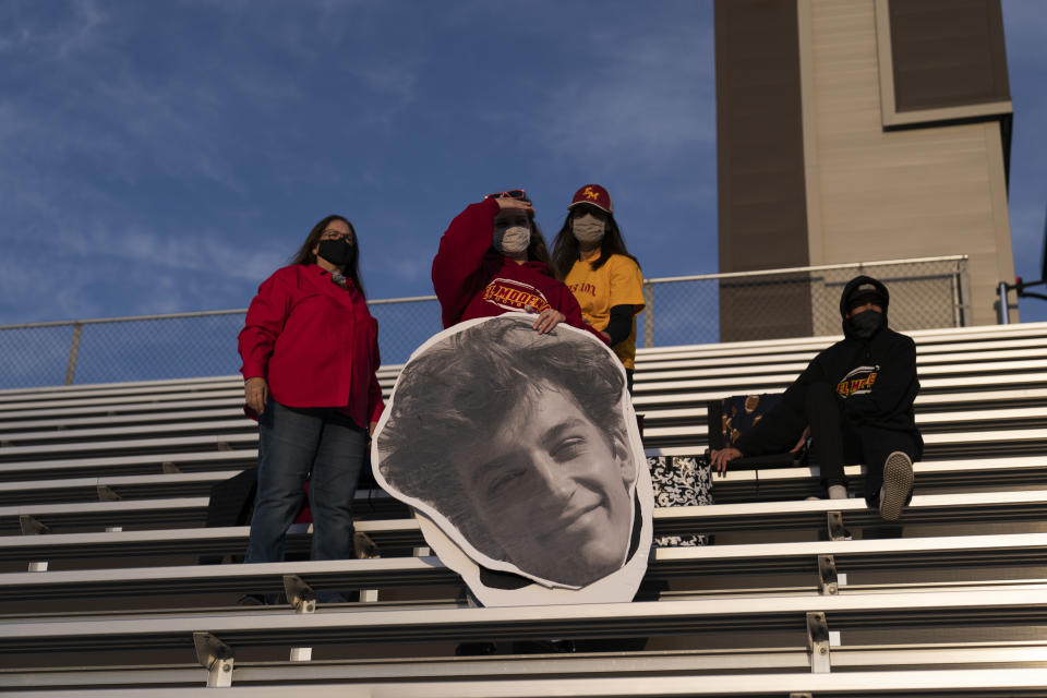 Anna Smith, center left, tries to spot her brother, an El Modena running back, while holding a cutout of him before the team's high school football game against El Dorado in Orange, Calif., Friday, March 19, 2021. "I love coming to watch my brother play," said Smith. "He's been working hard like everybody else. He's been really excited to finally get out and play." (AP Photo/Jae C. Hong)