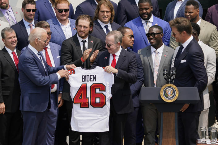 Tampa Bay Buccaneers quarterback Tom Brady, right, looks on as Tampa Bay Buccaneers co-owner Bryan Glazer hands President Joe Biden a jersey during a ceremony on the South Lawn of the White House, in Washington, Tuesday, July 20, 2021, the president honored the Super Bowl Champion Tampa Bay Buccaneers for their Super Bowl LV victory. (AP Photo/Andrew Harnik)