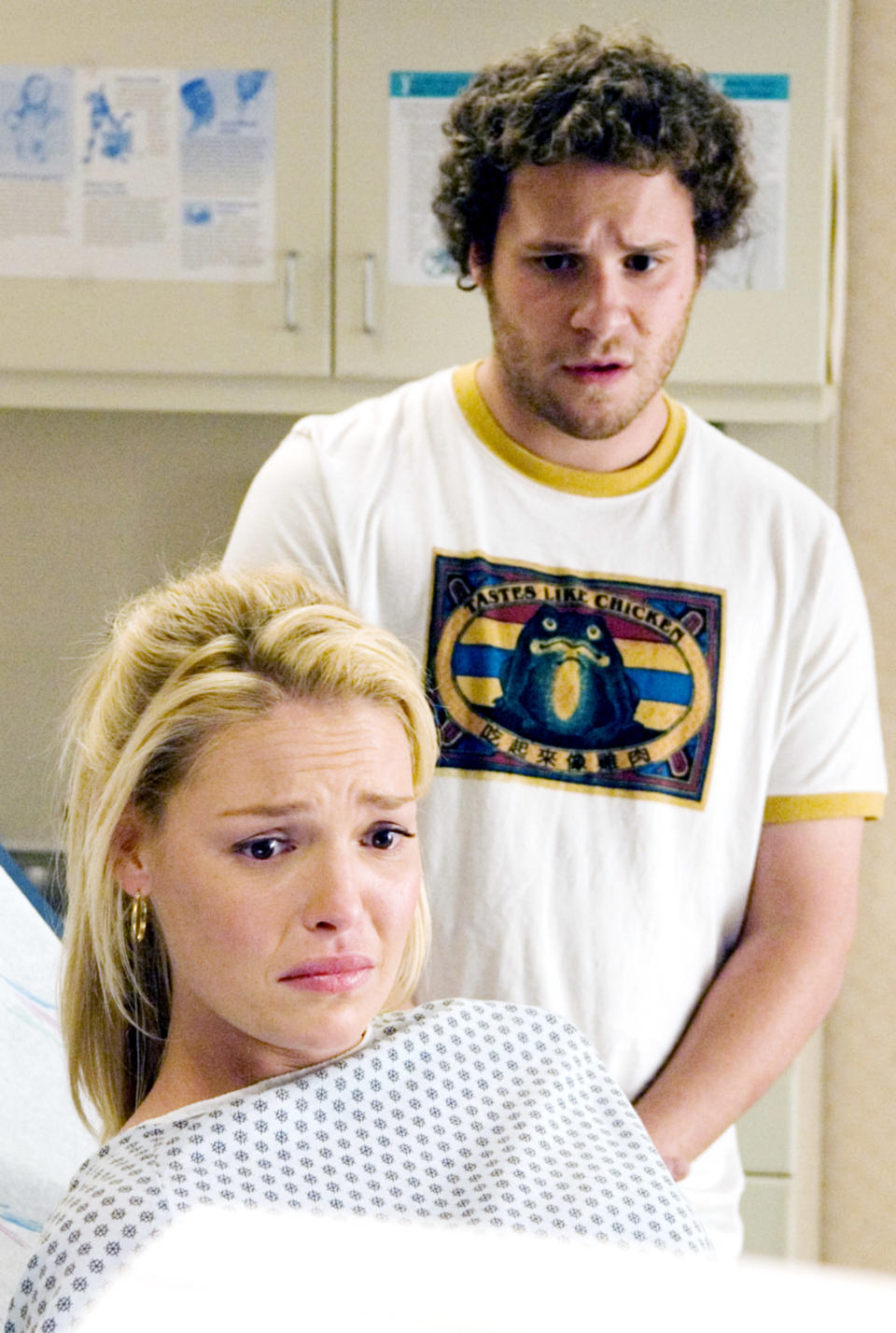 Katherine Heigl looking distressed in a hospital gown with Seth Rogen standing behind her, appearing concerned, in a medical setting