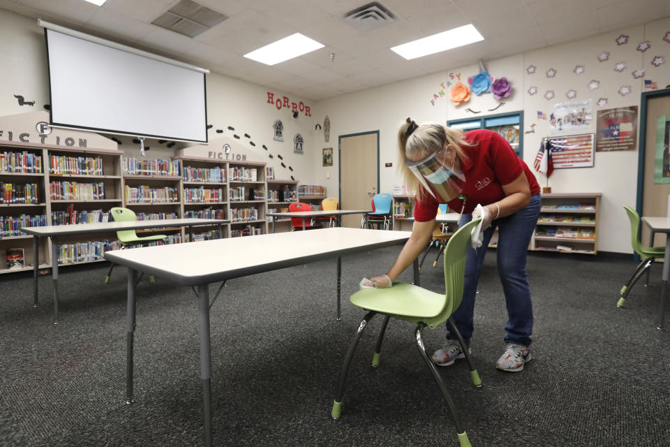 Wearing a mask and face guard as protection against the spread of COVID-19, Garland Independent School District custodian Maria Concha wipes down a chair in the library at Stephens Elementary School in Rowlett, Texas, Wednesday, July 22, 2020.(AP Photo/LM Otero)
