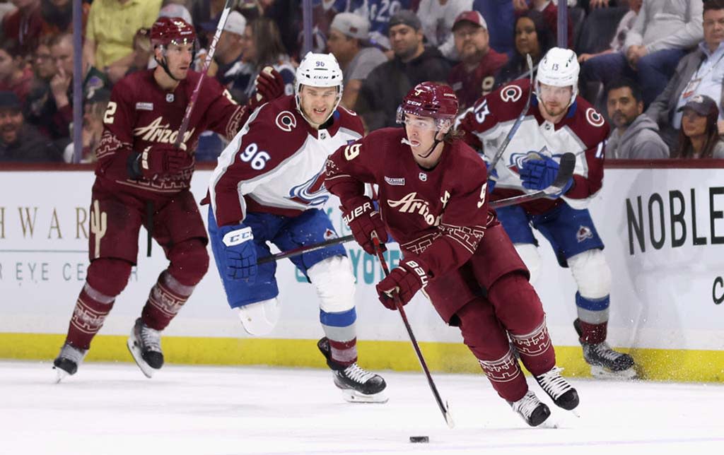  Clayton Keller of the Arizona Coyotes skates with the puck ahead of Mikko Rantanen of the Colorado Avalanche . 