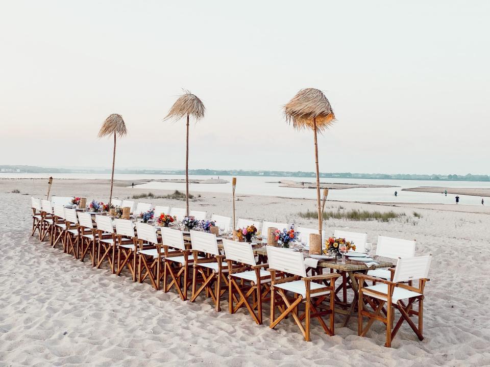 a tablescape on the beach featuring white chairs and a long table