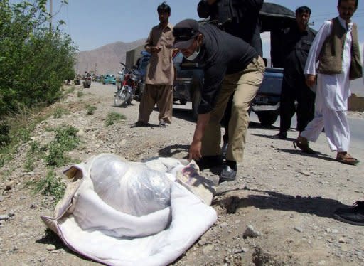 A Pakistani policeman looks at the dead body of British aid worker Khalil Rasjed Dale (L), found wrapped in a bag on a road side in Quetta on April 29, 2012