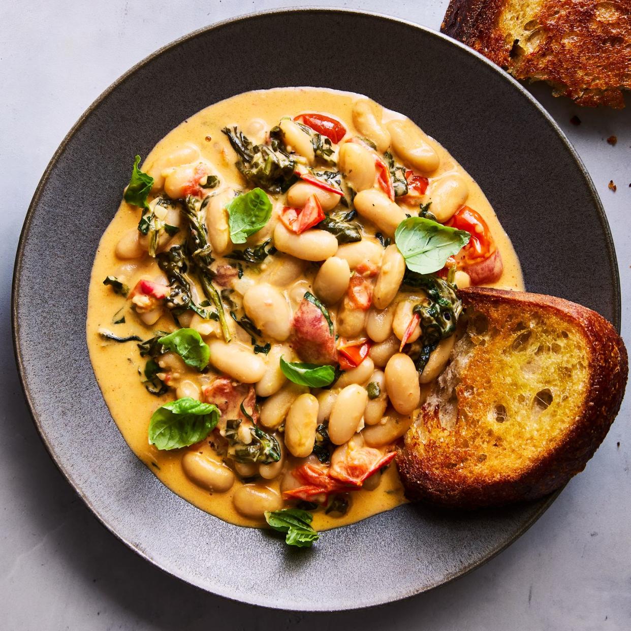 creamy tuscan white beans on a grey plate topped with basil, with toast alongside