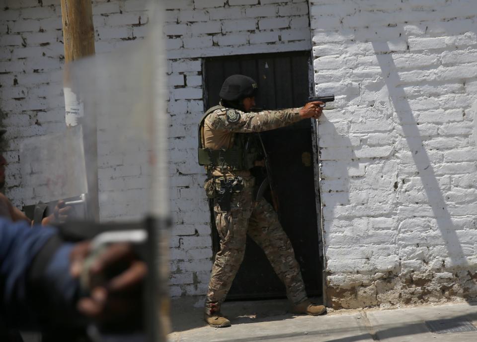 A police officer aims his weapon at supporters of ousted Peruvian President Pedro Castillo, during a protest against his detention, in Chao, Peru, Thursday, Dec. 15, 2022. Peru's new government declared a 30-day national emergency on Wednesday amid violent protests following Castillo's ouster, suspending the rights of "personal security and freedom" across the Andean nation. (AP Photo/Hugo Curotto)