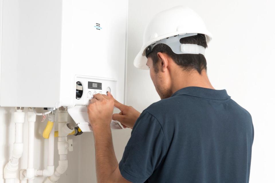 A technical service staff member in a white hard hat tinkers with a water heater.