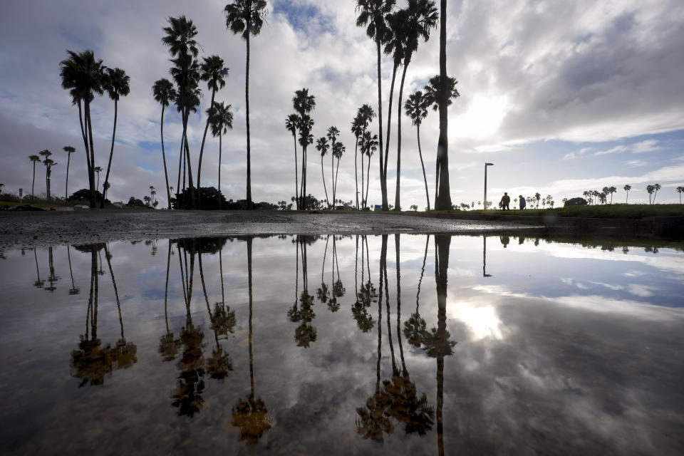 FILE - Two people walk along Mission Bay during a break in the rain on Feb. 1, 2024, in San Diego. California's current rainy season got off to a slow start but has rebounded with recent storms that have covered mountains in snow and unleashed downpours, flooding and mudslides. The water content of the vital Sierra Nevada snowpack has topped 80% of normal to date while downtown Los Angeles has already received more than an entire year's average annual rainfall. (AP Photo/Gregory Bull, File)