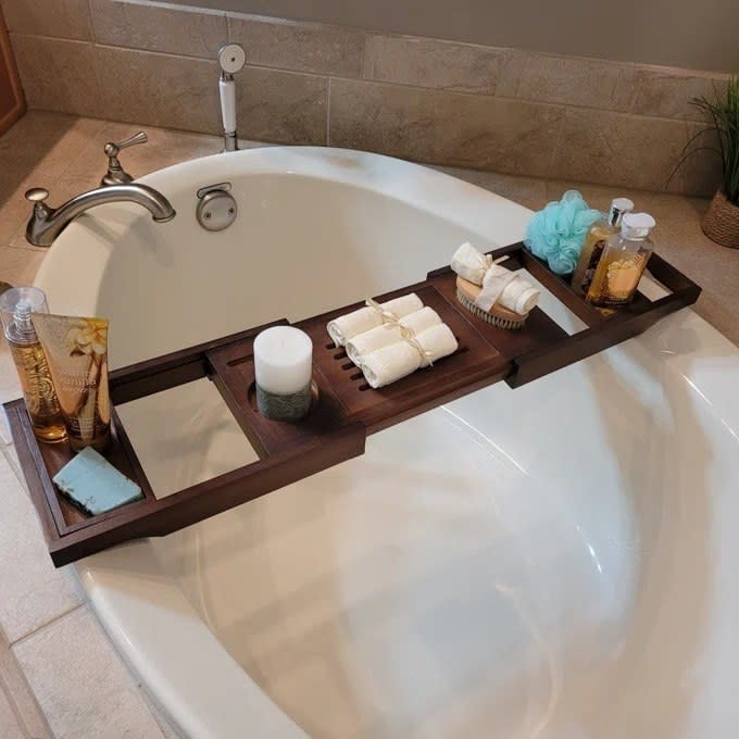 A reviewer photo of the bath caddy holding multiple items over a bathtub