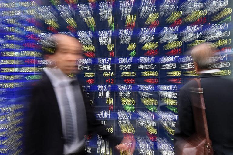 Local businessmen pass by a share pricers board in Tokyo, on November 11, 2014