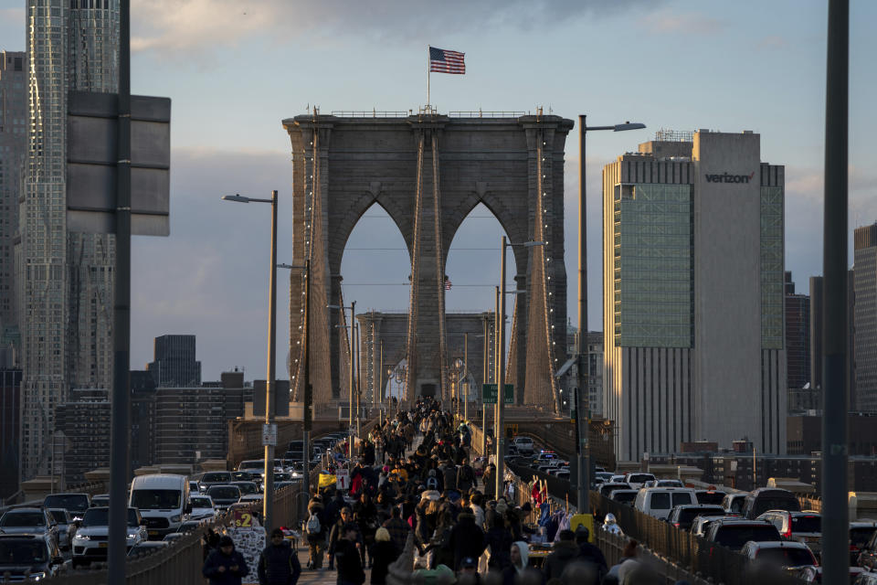 FILE - People walk on the Brooklyn Bridge at sunset, Friday, Nov. 18, 2022, in New York. Around Manhattan and elsewhere in the city, hotels that served tourists just a few years ago have become de facto emergency shelters. The latest is the historic Roosevelt Hotel in midtown Manhattan, which shuttered three years ago, is reopening later this week as a welcome center and shelter for asylum seekers. (AP Photo/Julia Nikhinson, File)