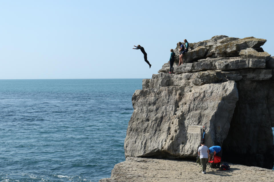 A person is jumping from the Limestone Sea Stack, next to Portland lighthouse on the Isle of Portland, Jurassic Coast, Dorset, England, UK. The person is partaking in the dangerous sport of tombstoning which is being watched by spectators. August, 29, 2021.