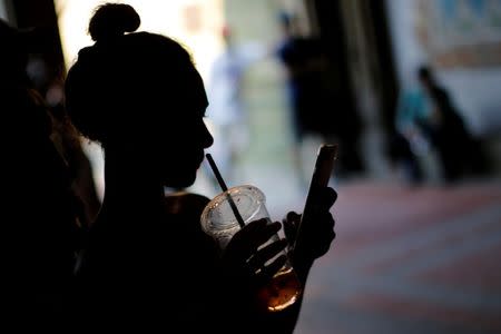 A woman holds a drink while using her mobile phone on a hot summer day in Central Park, Manhattan, New York, U.S., July 01, 2018. REUTERS/Eduardo Munoz