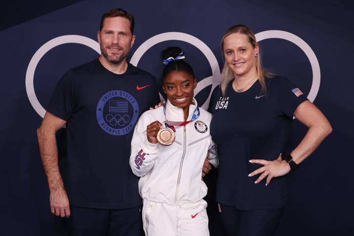 Simone posing with her coaches for a photo and holding up her bronze medal