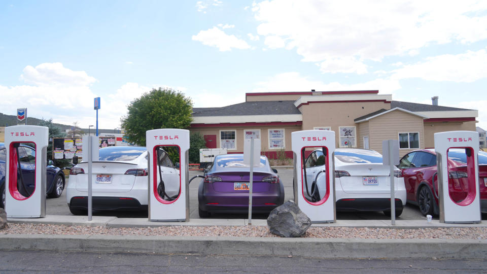 Five Tesla cars charge up at an outdoor Tesla station.