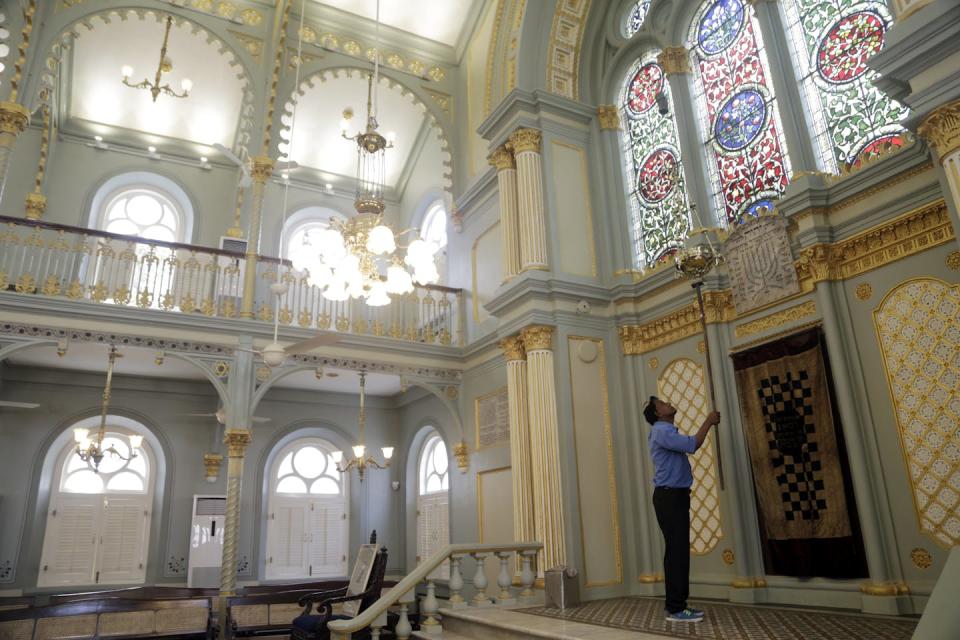 A man in a blue shirt holds up a long tool inside an airy room with stained glass windows.